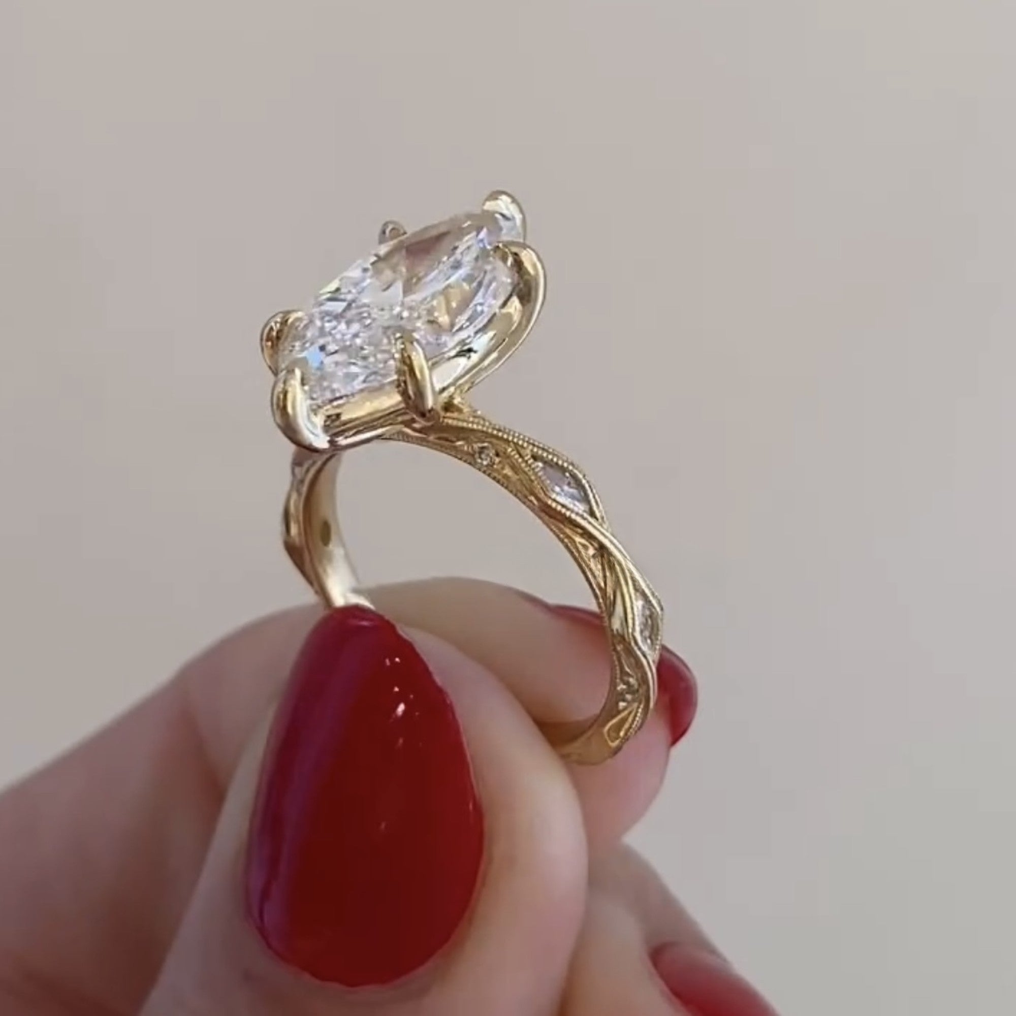 Gold ring with a large diamond held by a hand with red nail polish on a light 