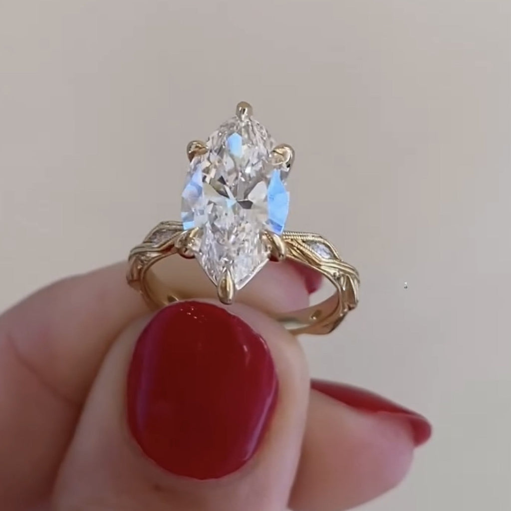 Gold ring with a large diamond held by a hand with red nail polish on a light 