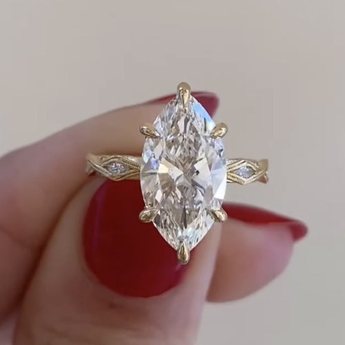 Gold ring with a large diamond held by a hand with red nail polish.