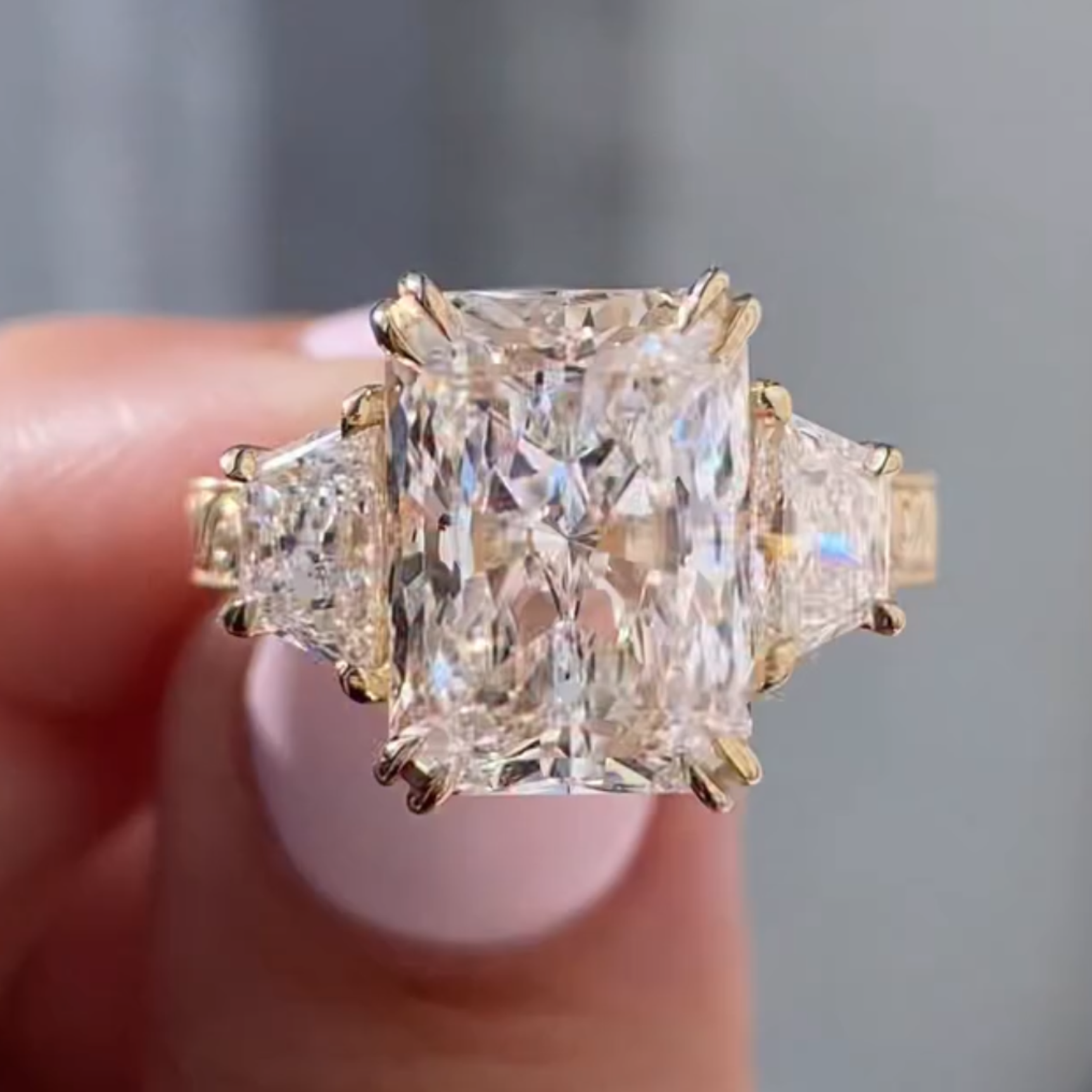 Gold ring with large diamond held between fingers against 