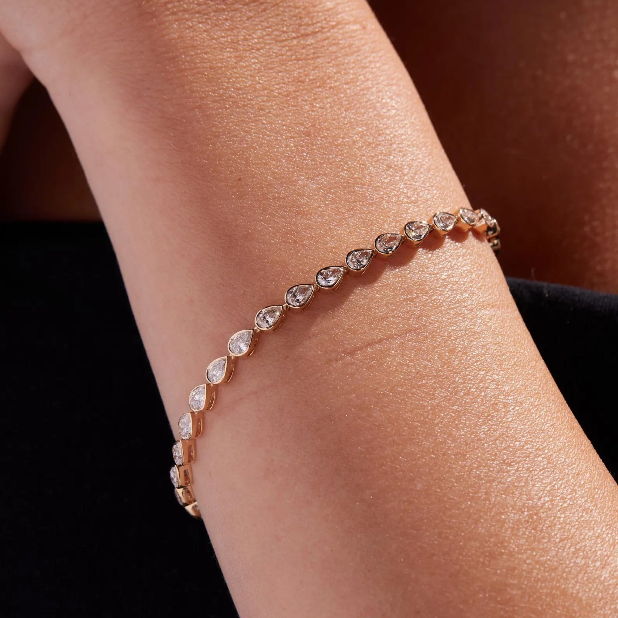 Rose gold bracelet with heart-shaped diamonds on a wrist against a dark 