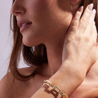 Close-up of a woman wearing a gold bracelet on a plain 