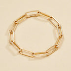 Gold chain bracelet with embedded stones on a beige 