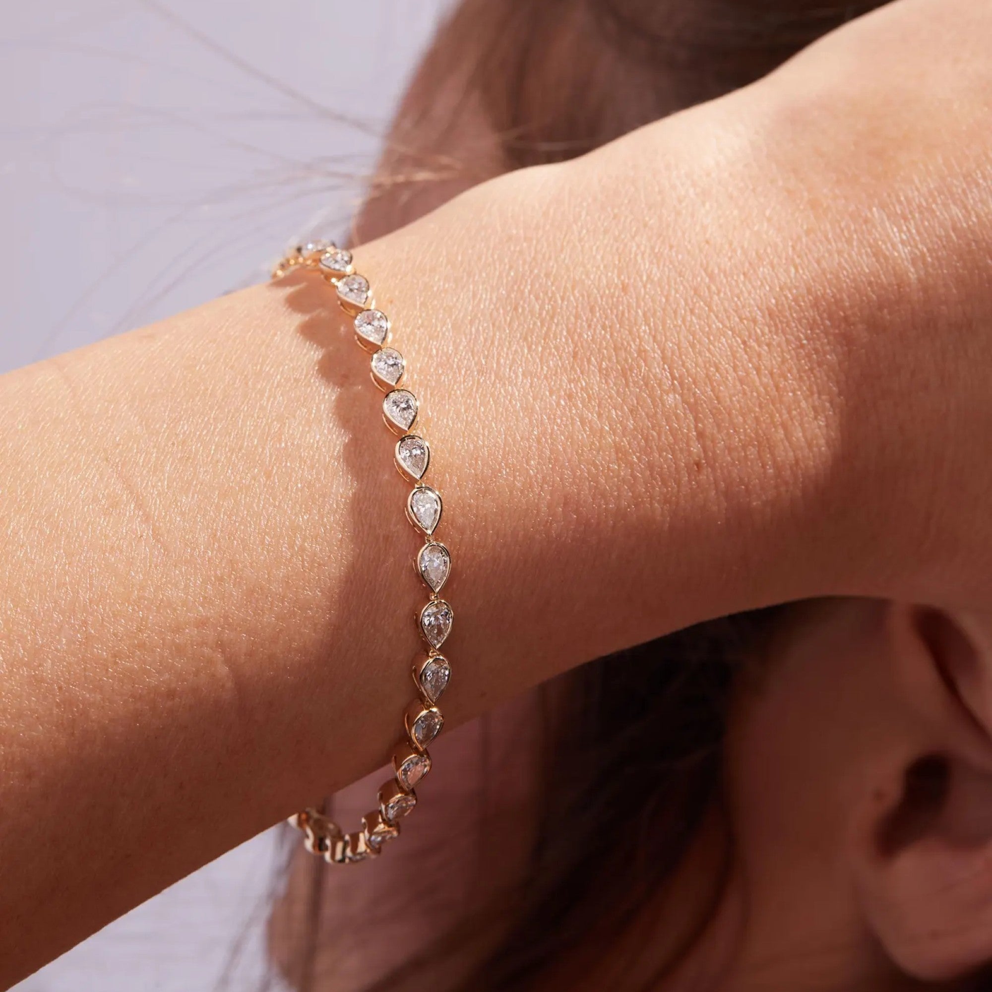 Rose gold bracelet with heart-shaped diamonds on a wrist against a neutral 