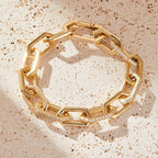 Gold chain bracelet with diamond accents on a textured beige surface