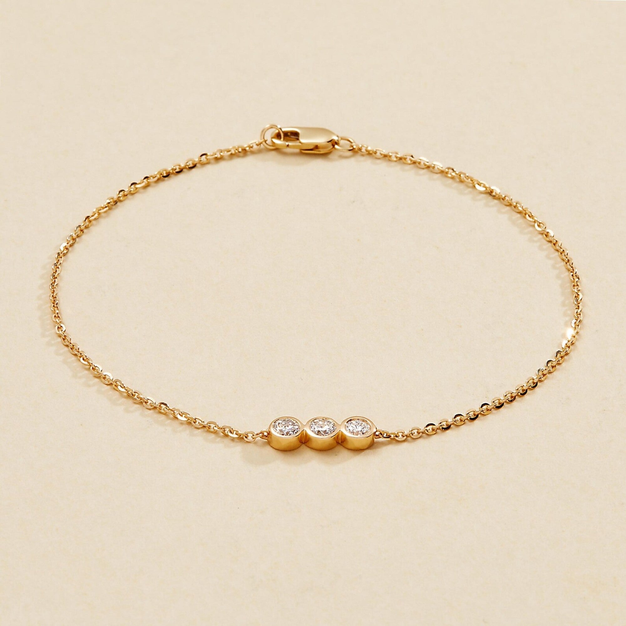 Gold bracelet with three small round diamonds on a beige 