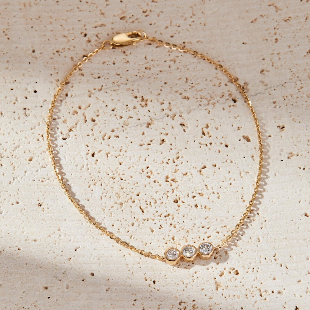 Gold bracelet with three clear stones on a textured beige surface
