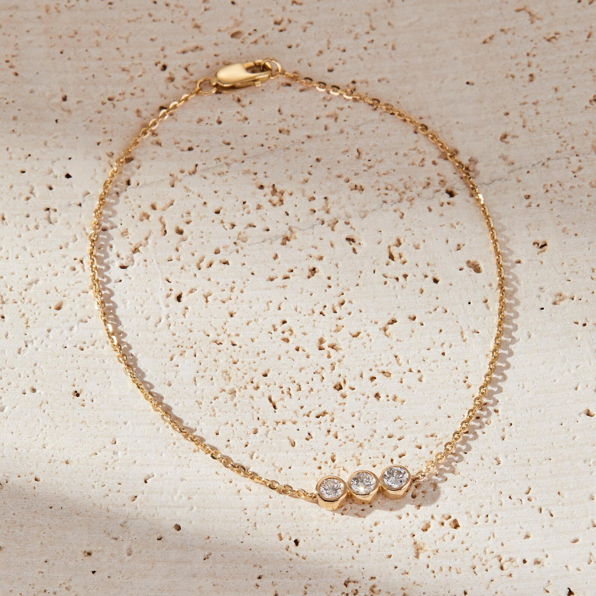 Gold bracelet with three clear stones on a textured beige surface