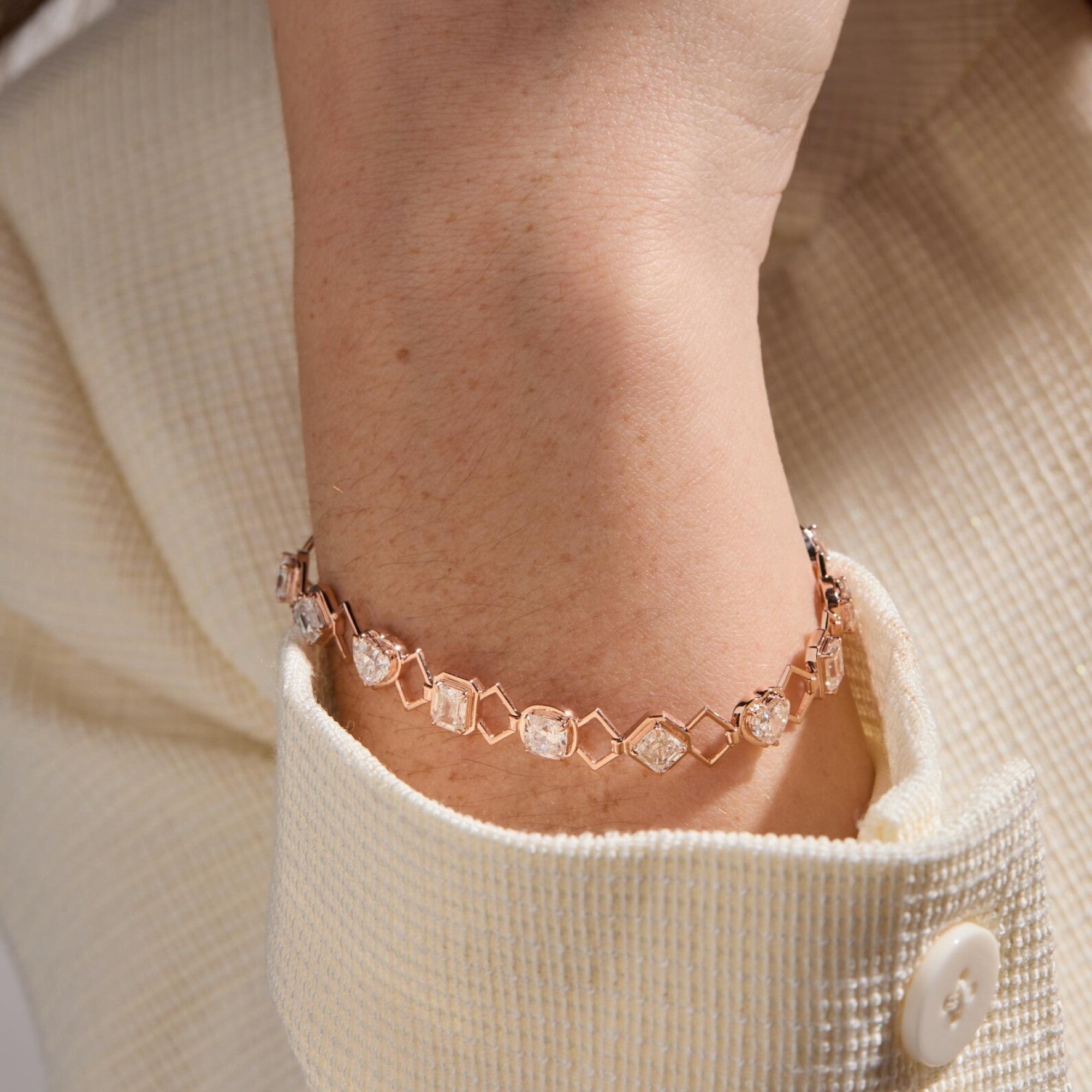 Rose gold bracelet with gemstones on a wrist, wearing a beige sweater.