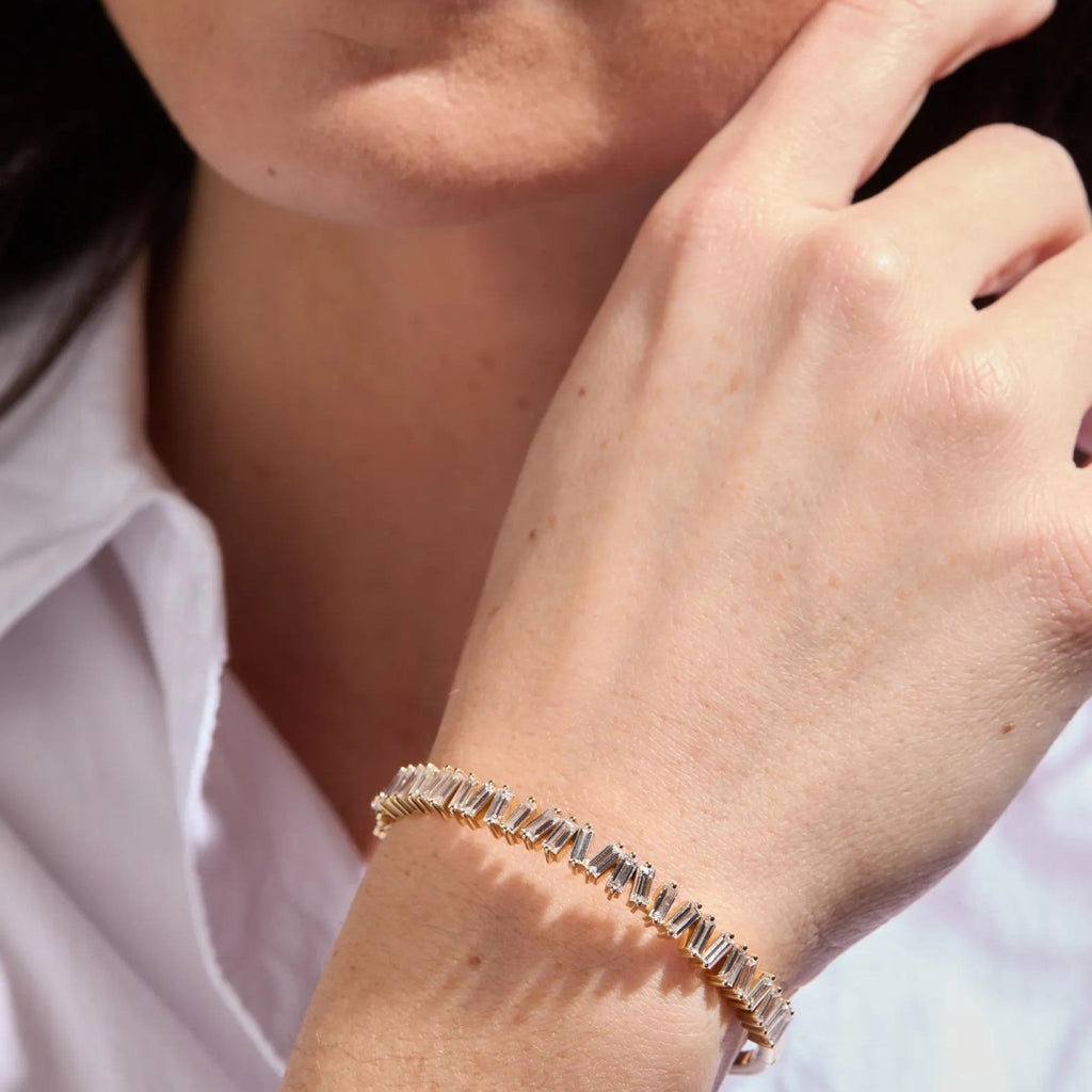 Close-up of a person wearing a gold bracelet on a white shirt.