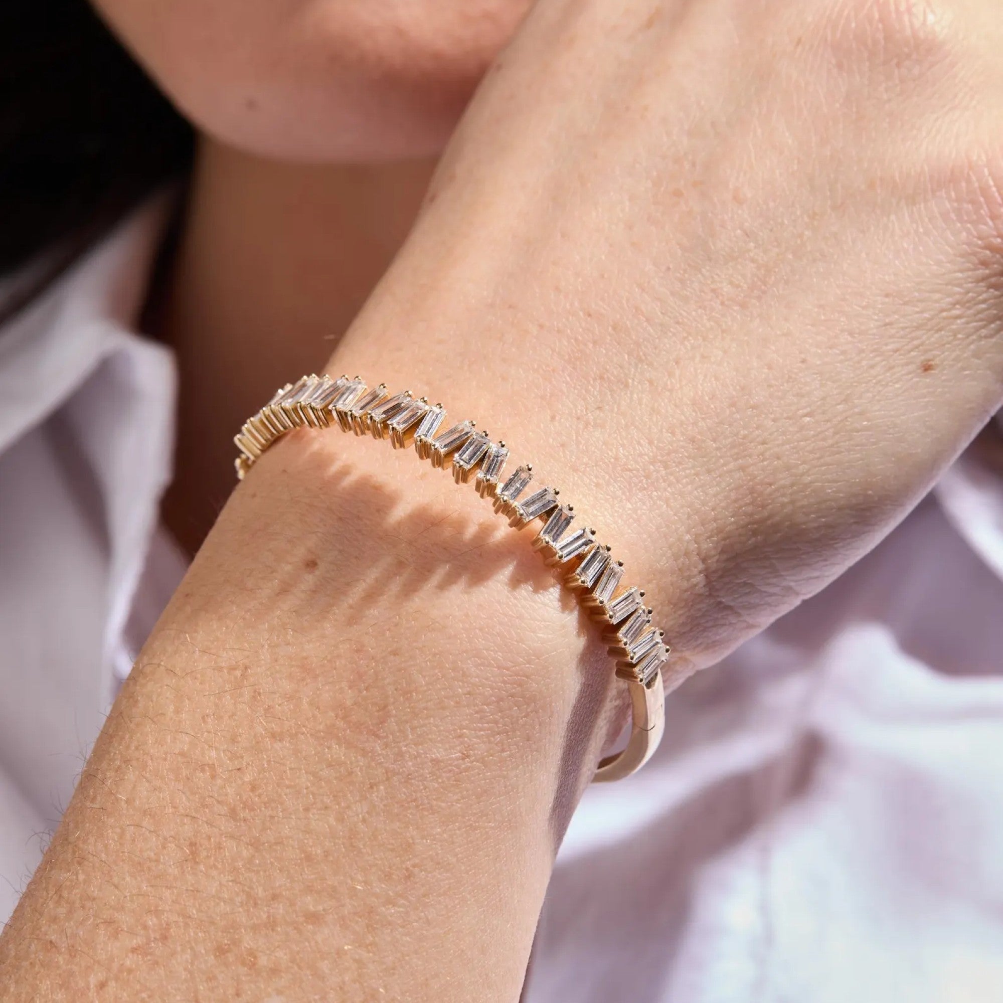 Rose gold bracelet with baguette diamonds on a wrist against a blurred 
