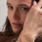 Close-up of a woman wearing a delicate bracelet with a diamond on a neutral 