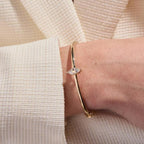 Gold bracelet with a clear gemstone on a wrist against a neutral background