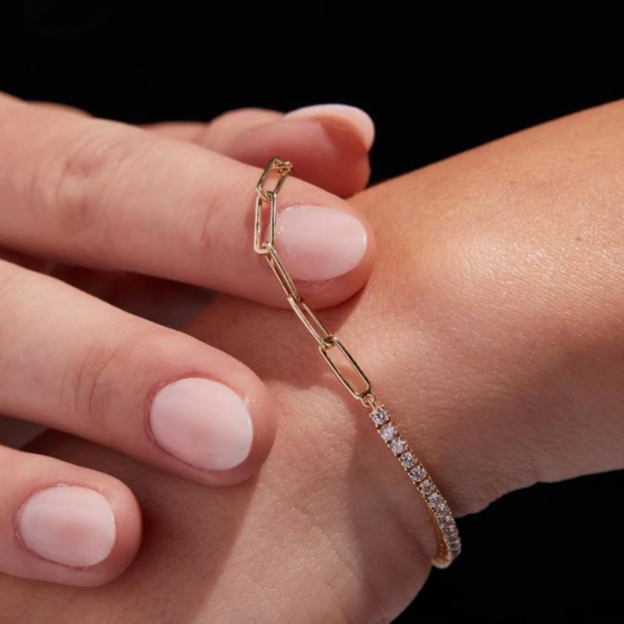 Close-up of a hand wearing a delicate gold bracelet with clear stones on a 
