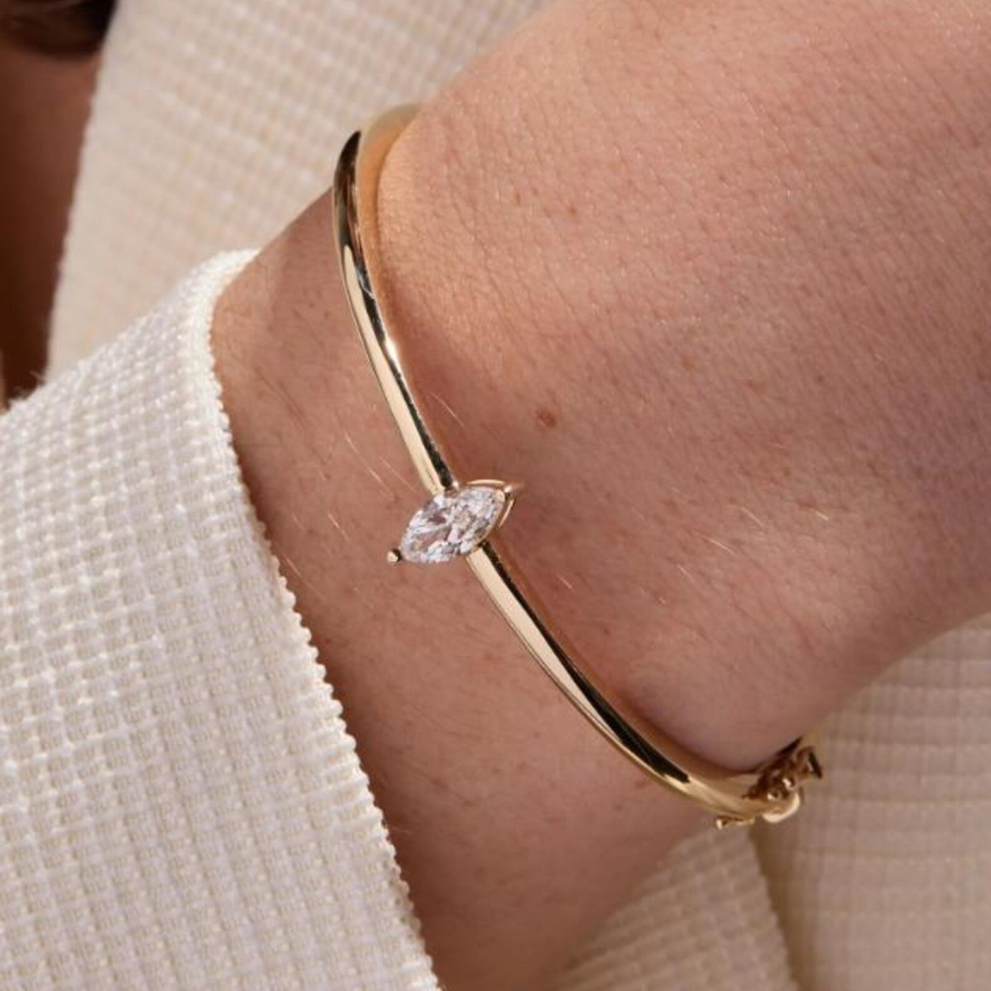 Gold bracelet with a diamond on a wrist against a neutral 
