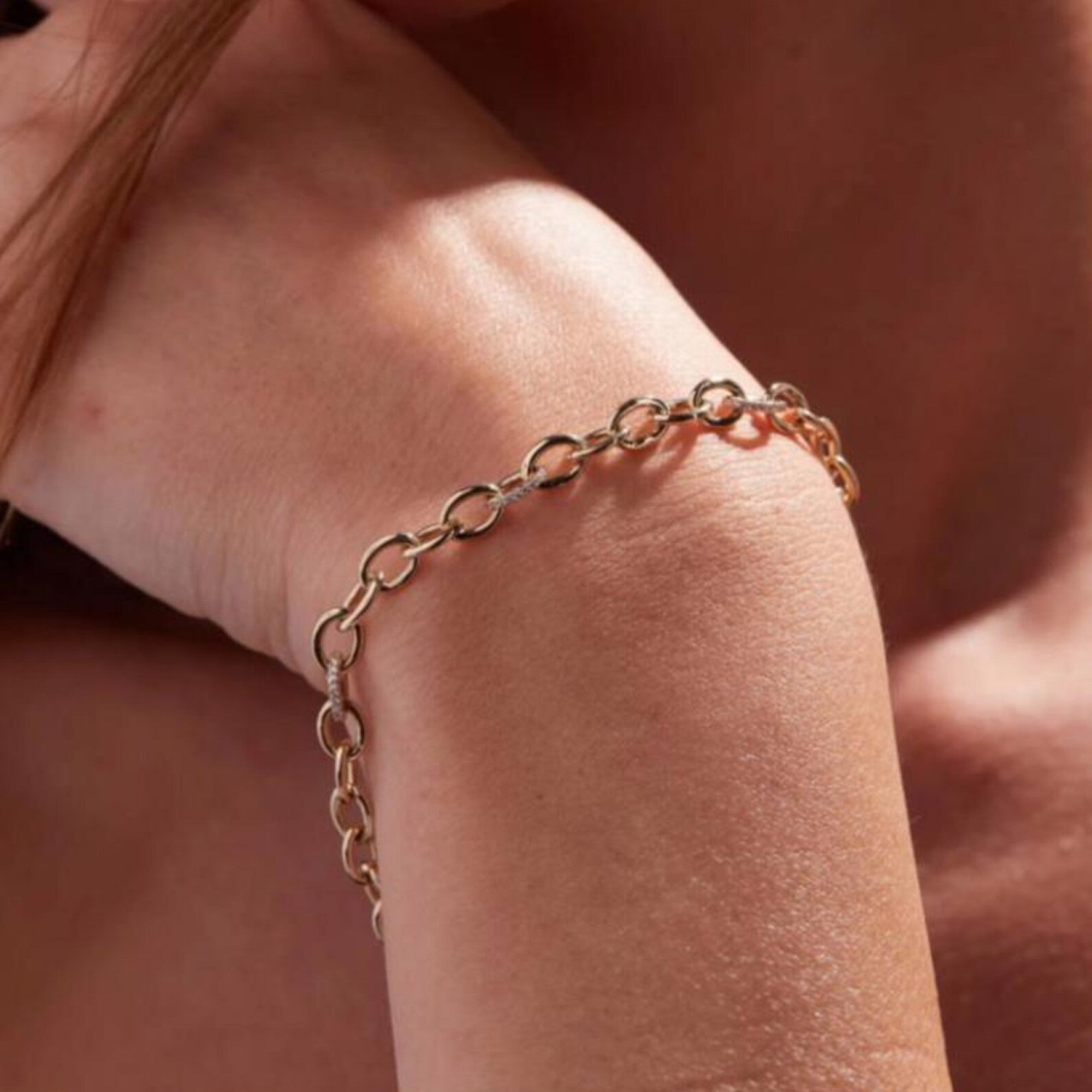 Gold chain bracelet on a person's wrist against a blurred 