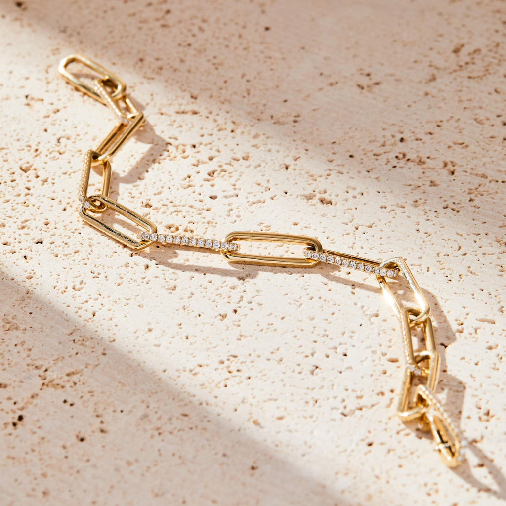 Gold chain bracelet with diamond accents on a beige surface