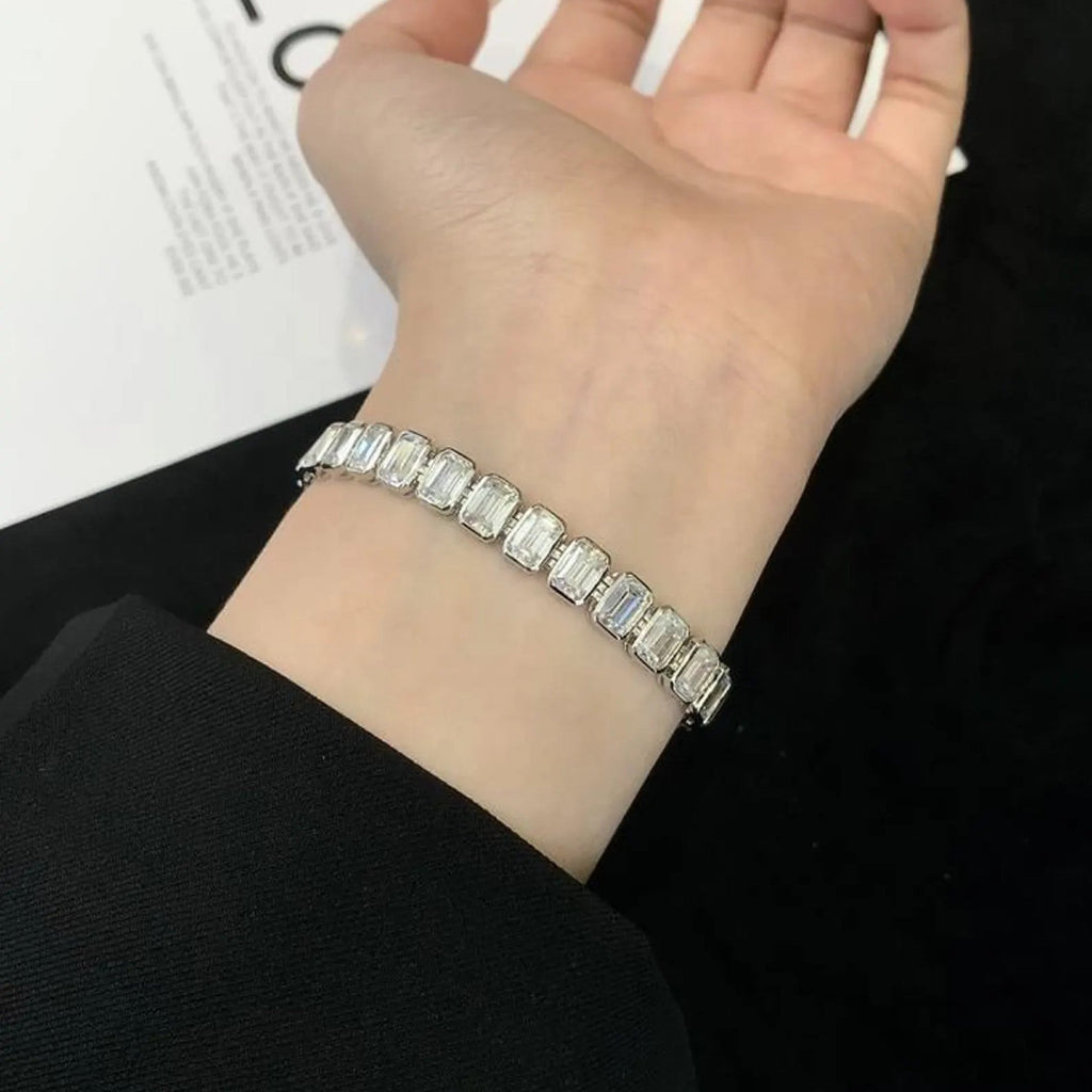 Silver bracelet with emerald-cut gemstones on a wrist, against a blurred 